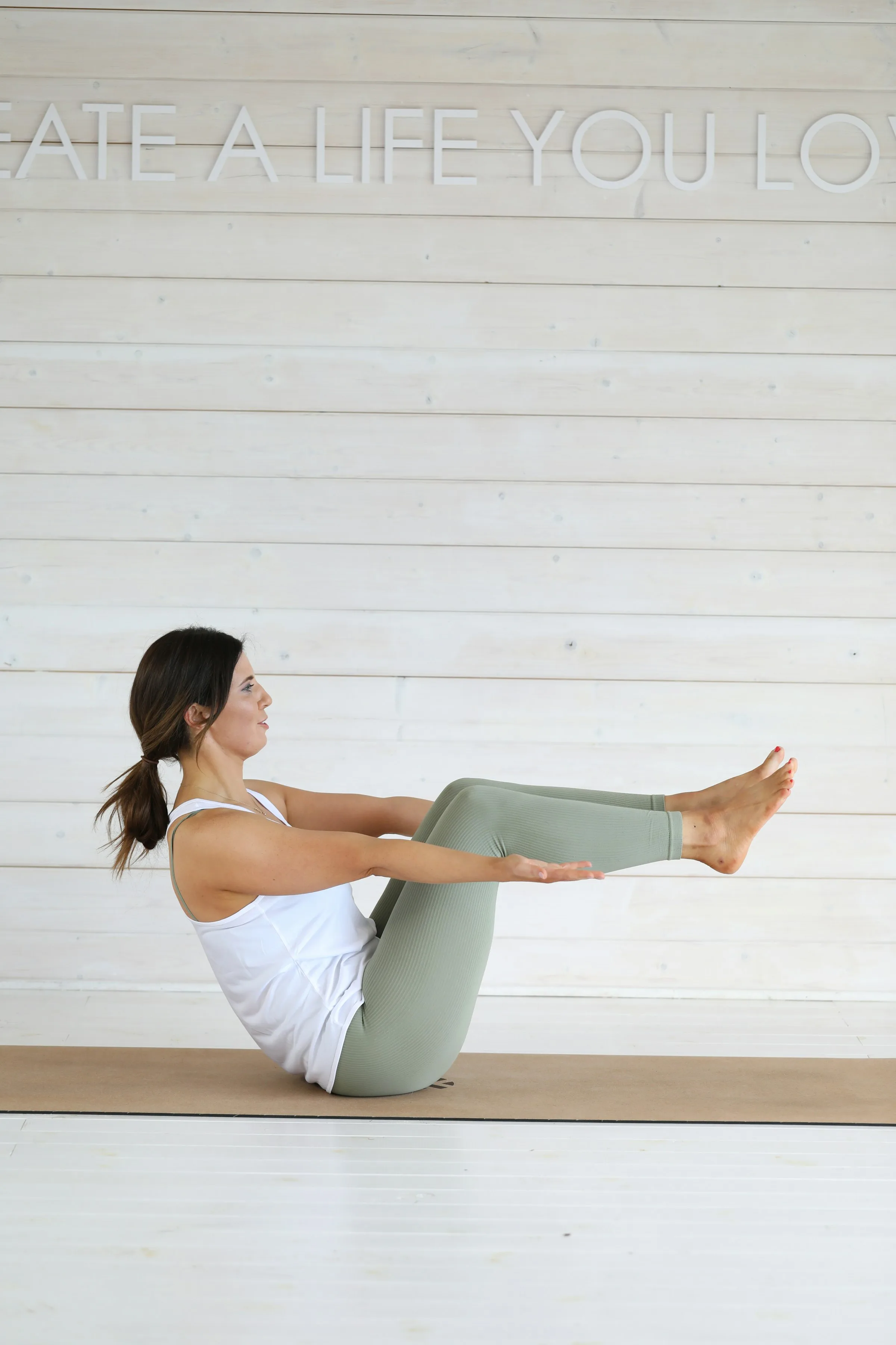 Allieva in equilibrio con le gambe sollevate, a tappetino, davanti a una parete bianca
